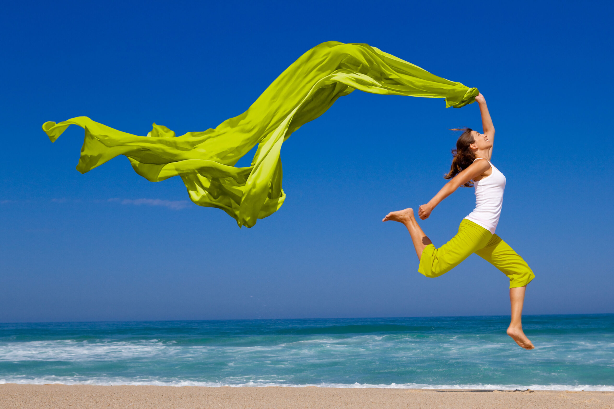Beautiful young woman jumping on the beach with a colored tissue